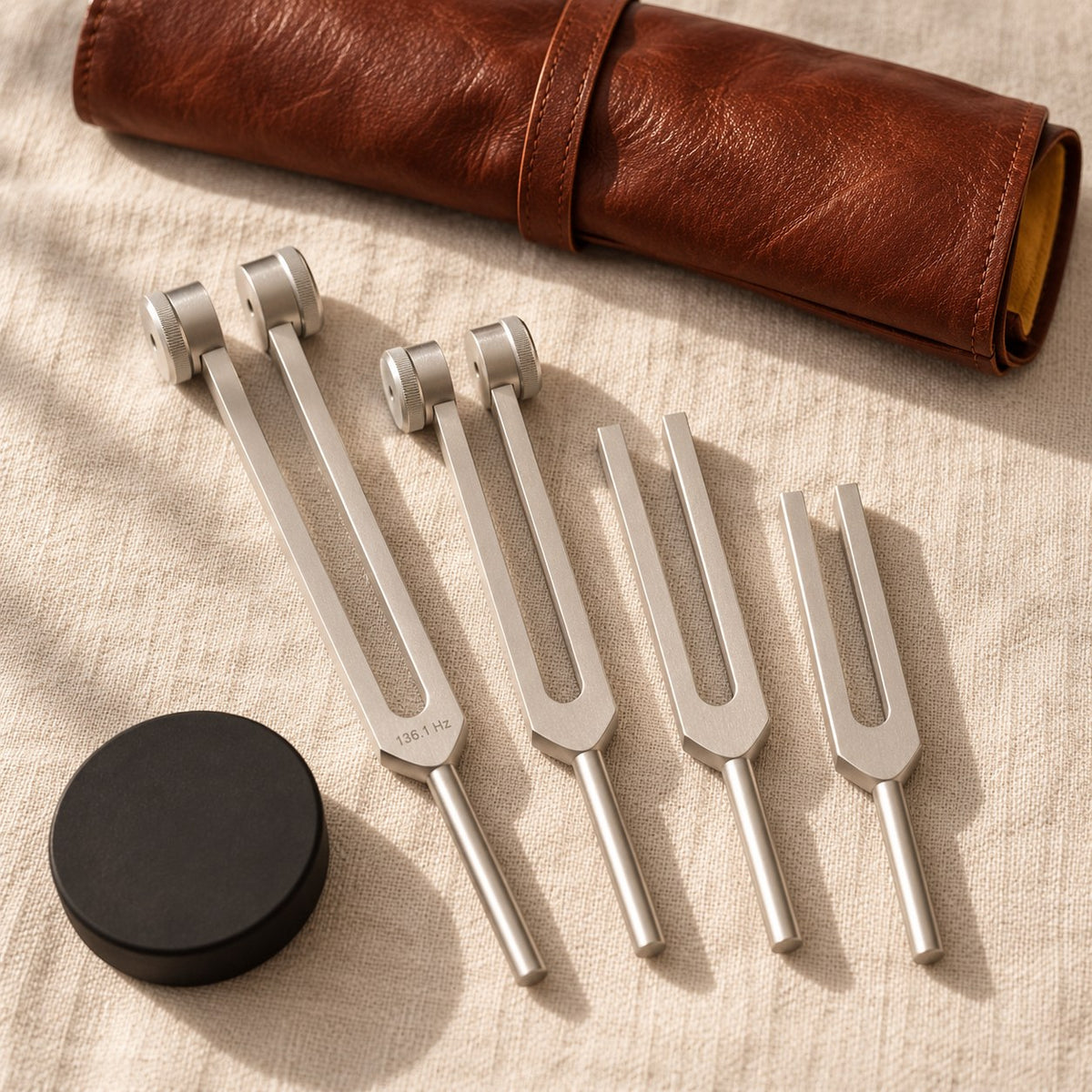 King Healing tuning fork set: two weighted and two unweighted aluminum forks, activator puck and leather roll pouch on linen